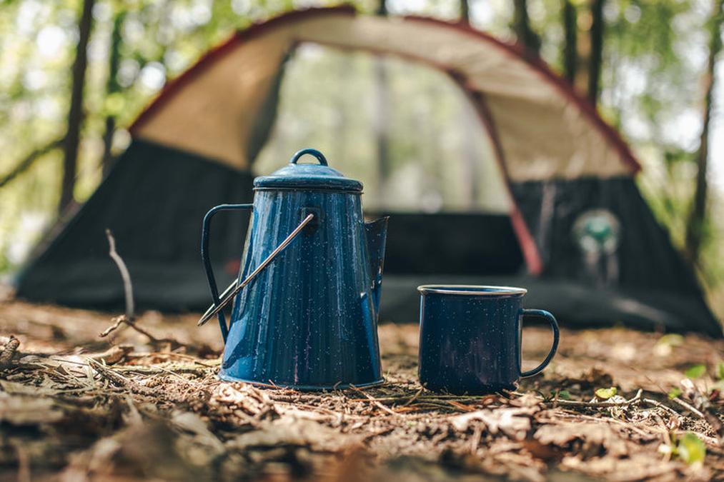 a blue coffee pot and a cup of coffee on a camping tent in the woods - camping kettle and coffee cup