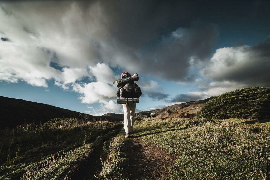 a man with a backpack and a backpack walking up a hill - Backpacker hiking in nature