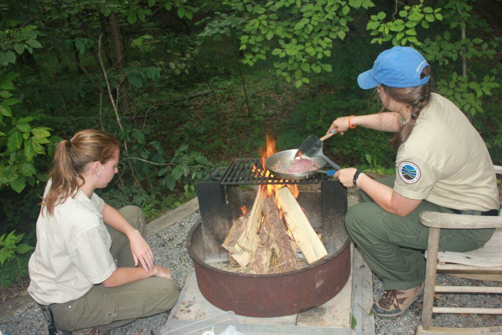 a woman sitting on a fire pit with a fire pit - File:Sky Meadows SM campfire cooking (19450684786).j